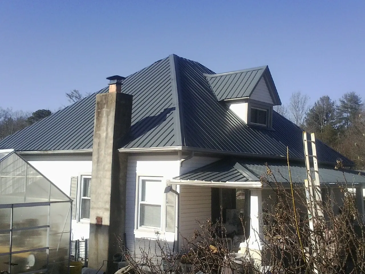 Dark blue standing seam metal roof on a white farmhouse with dormer — Slate & Tile Roof Repair by Roofing Brothers in Sibley