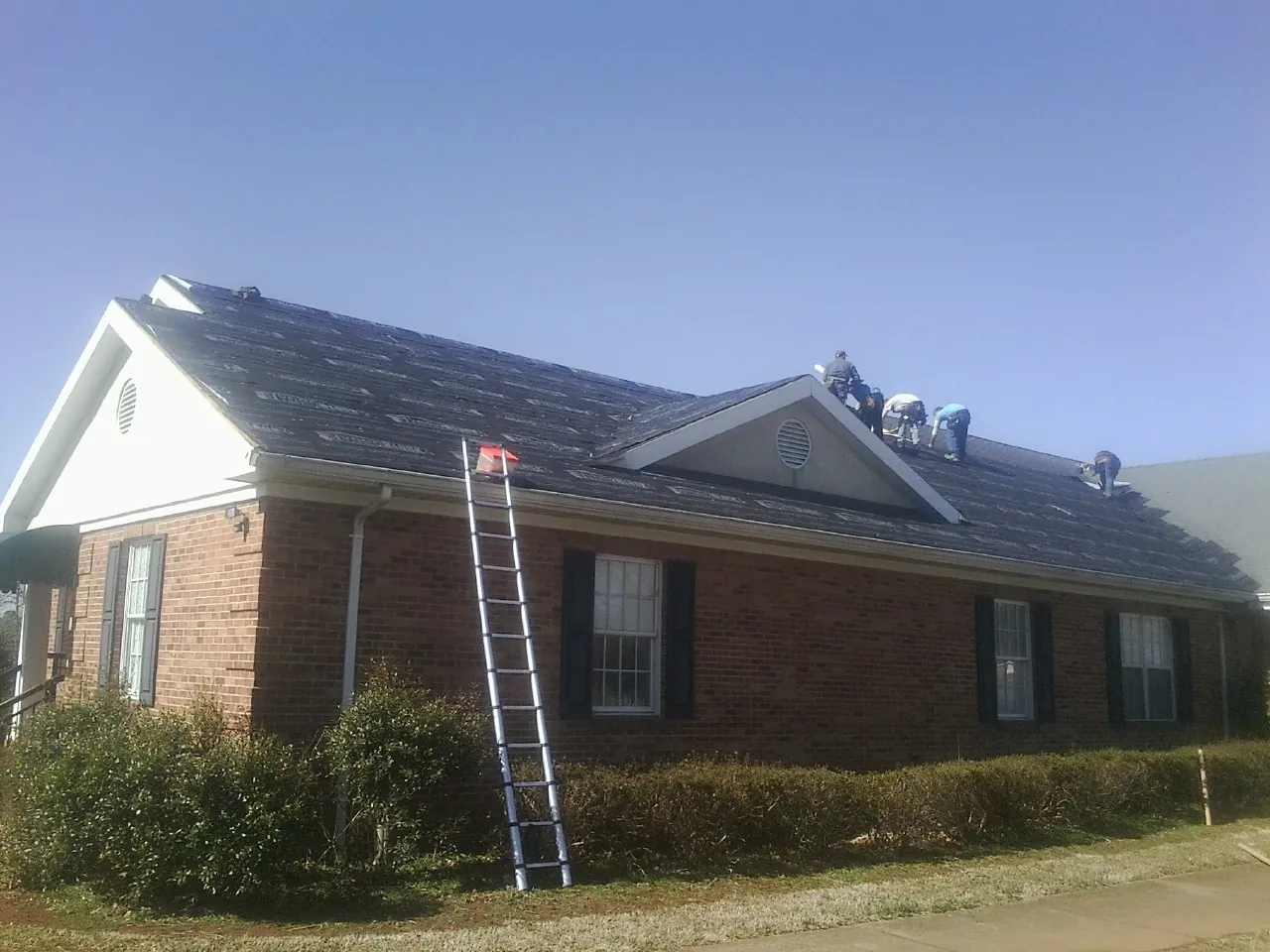 Crew tearing shingles off a brick ranch roof with a ladder set — Emergency Roof Repair work by our crew in Sibley