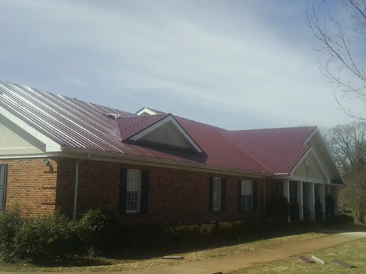 Red metal roof with gabled entries on a long brick building, from a Hail Damage Roof Repair job in Sibley