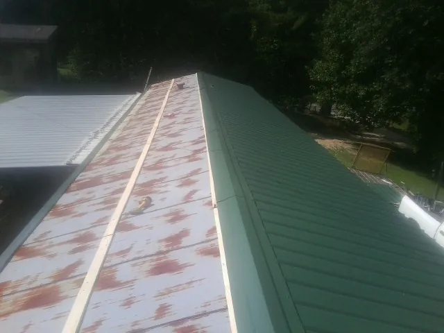 Old rusted panels beside newly installed green metal roofing — Wind Damage Roof Repair by Roofing Brothers in Sibley