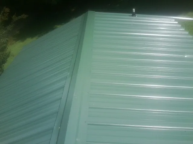 New green metal panels meeting at the ridge of a roof — Flat Roof Repair work by our crew in Sibley