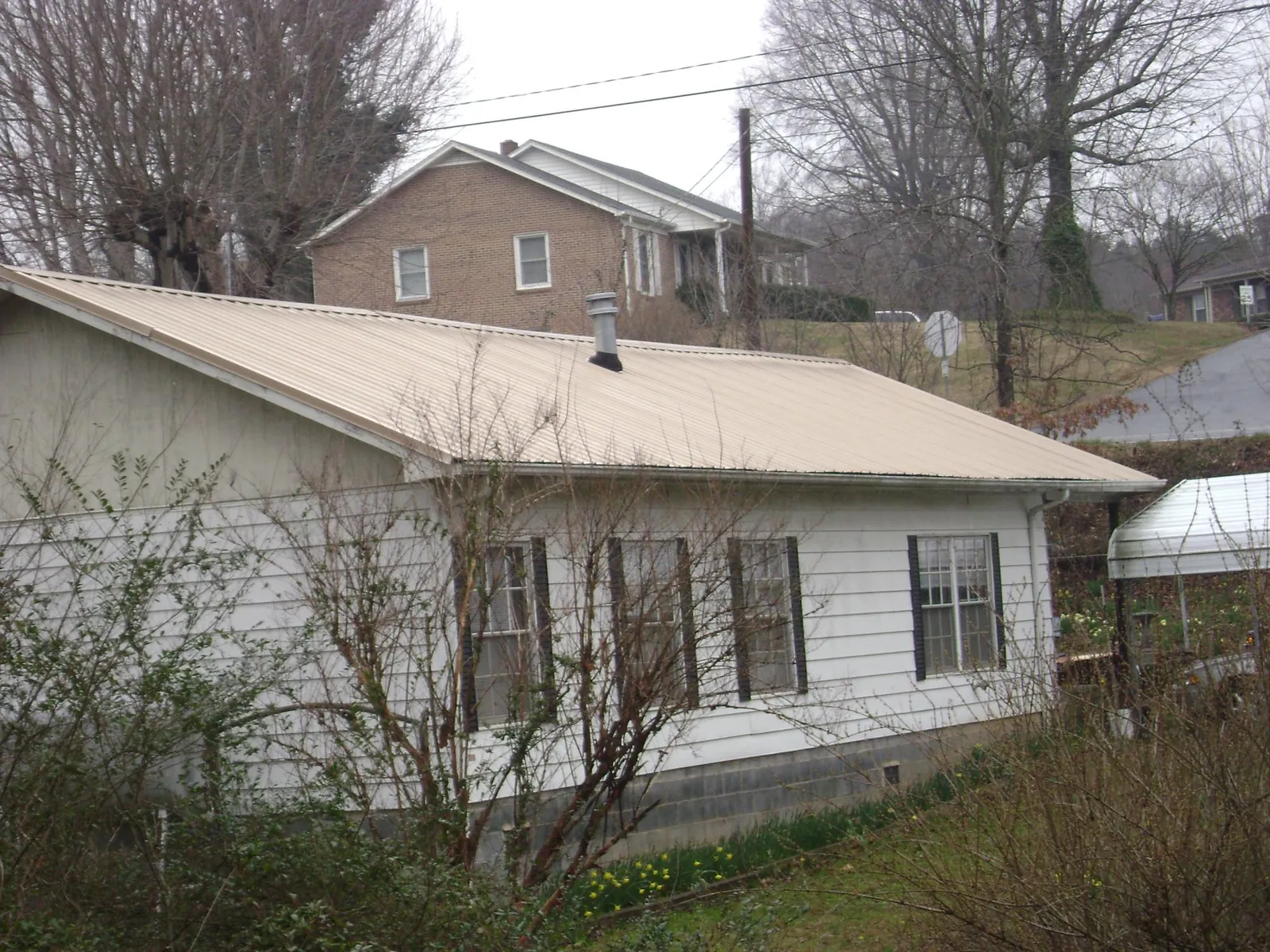 Tan metal roof on a white sided house set into a hillside — Commercial Roofing by Roofing Brothers in Sibley