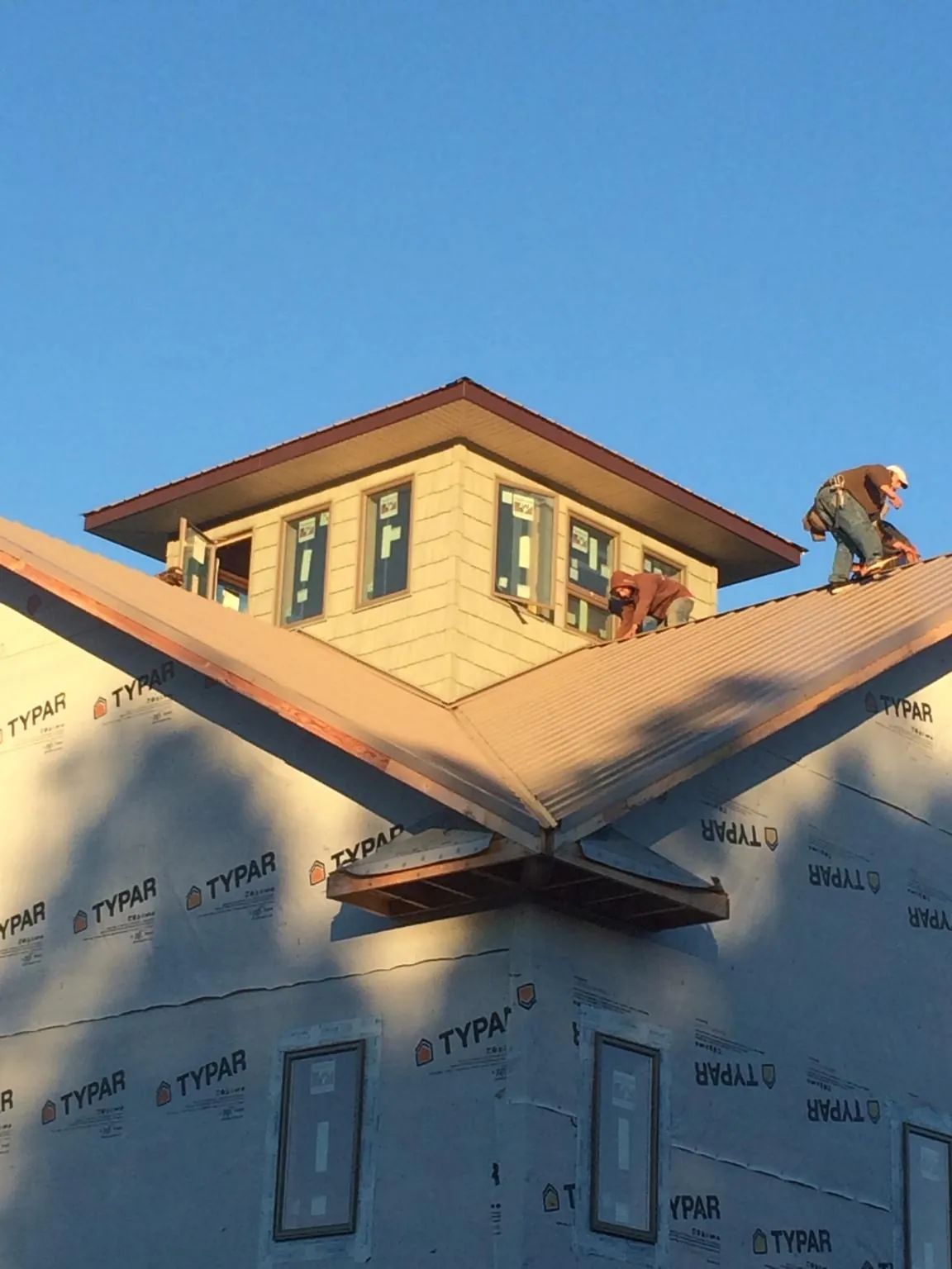 Roofers working around a rooftop cupola on a new metal roof at sunset — Roof Waterproofing in Sibley by Roofing Brothers